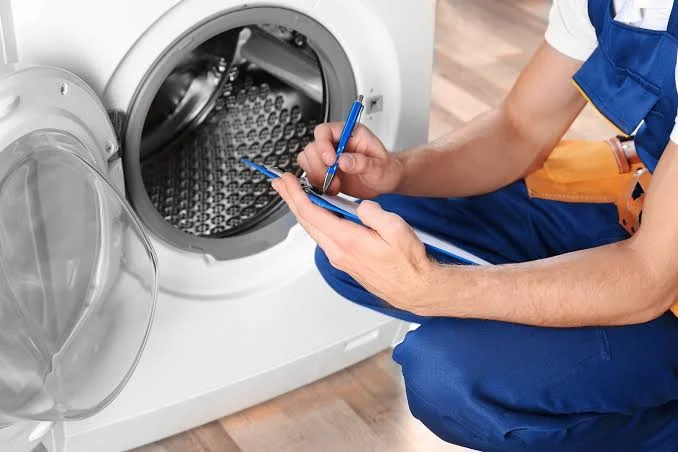 Appliance technician recording notes beside a washing machine