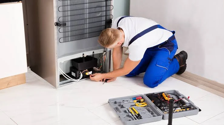 Technician inspecting the rear components of a refrigerator